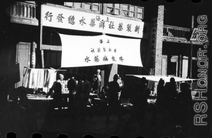 A large sign advertises for psoriasis lotion (牛皮癣水), and touts call out to passers-by in China. During WWII.  From the collection of Hal Geer.