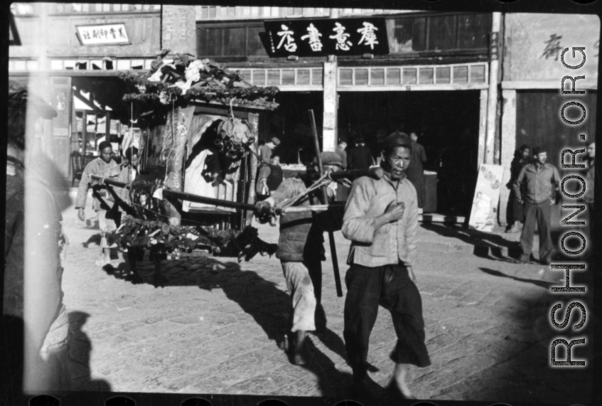 Men tote a decorated sedan chair used to carry the bride during weddings. In China, during WWII.