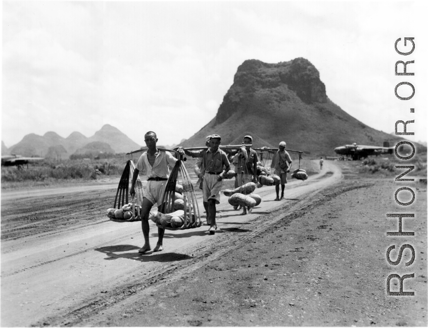 Men carrying gourds in Guilin, near the American air base, with karst mountains and B-25 bombers in the background. During WWII.  From the collection of Hal Geer.