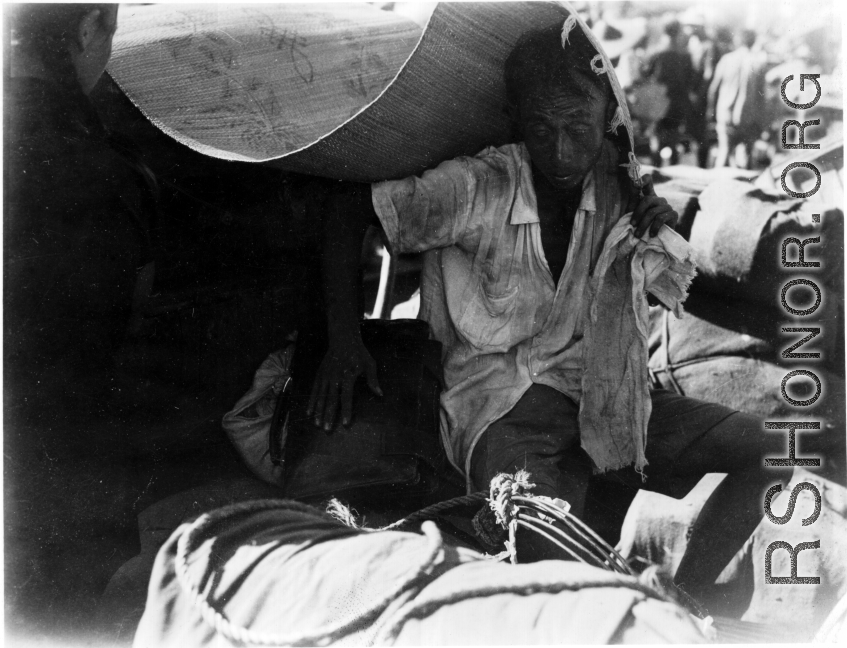 A refugee shields himself from the hot sun with a straw mat in Guangxi province, China, during WWII. Fall 1944.