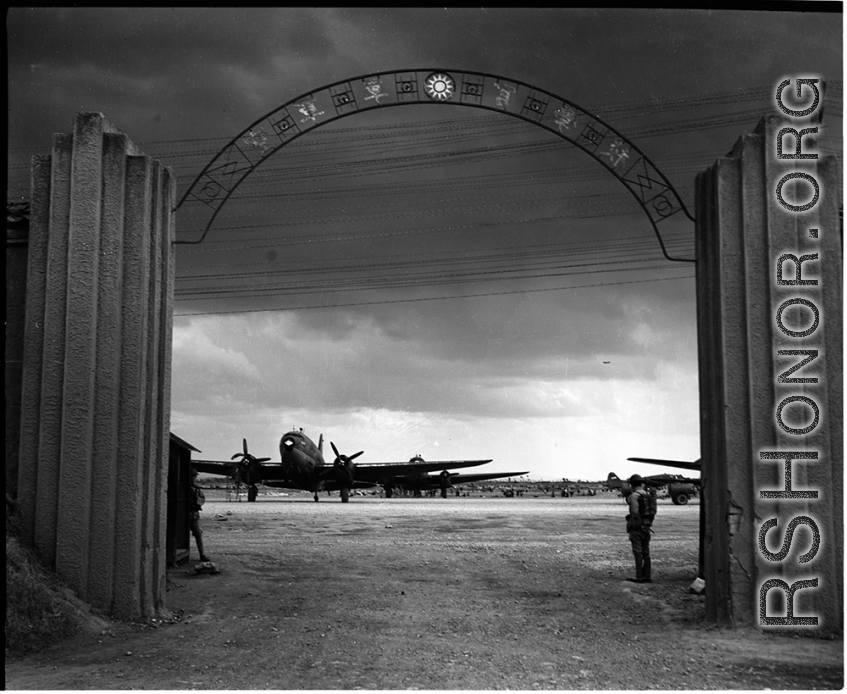 Guarded gates of the Nationalist Kunming Air Force Officer Training School during WWII, with C-46 transports, and a fuel trailer (on the far right).