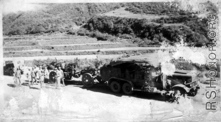 GIs and Chinese soldiers chat near a large Chinese transport truck towing a camouflaged artillery piece in SW China during WWII. 