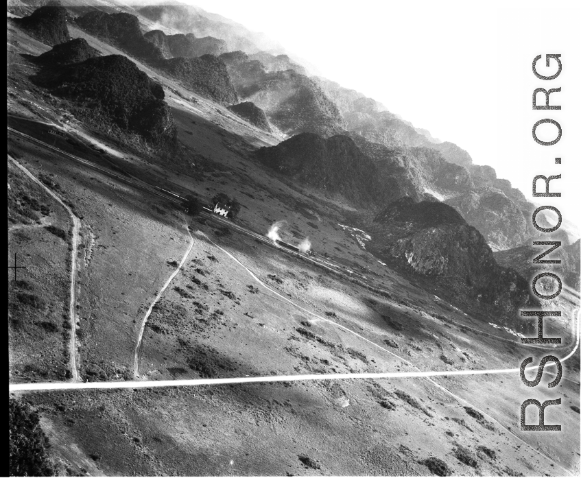 Smoke or steam arises from two railway cars in SW China, French Indochina, or Burma, in the CBI, during WWII, among karst peaks.