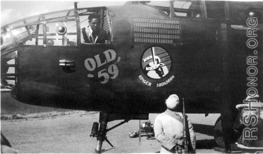 Lloyd Kershaw works in the bombardier's compartment of "Old 59". This B-25C of the 491st Bomb Squadron had completed 221 combat missions, as represented by the 'bomb' symbols painted above the Squadron's ' Ringers' insigne. Kershaw was preparing the aircraft for its trip back to the USA. An unidentified "Old 59" crew member stands beside a Chinese soldier, who would have been guarding the aircraft through the night.