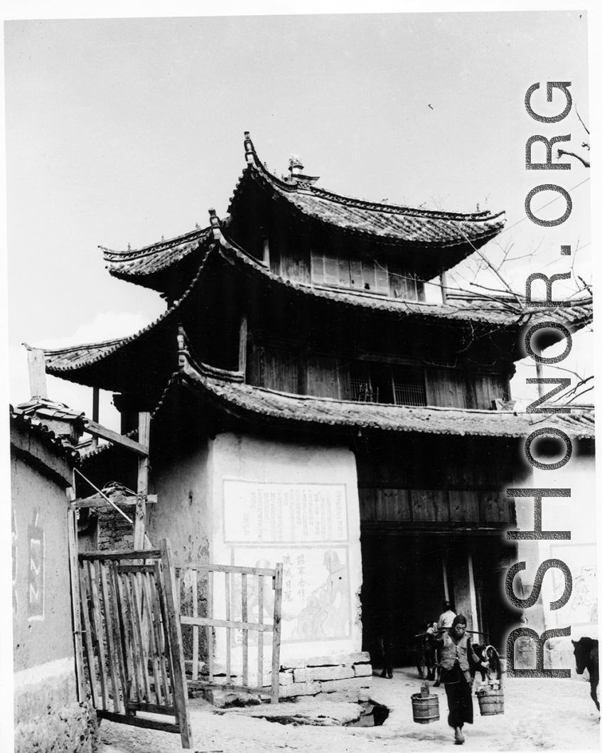 People come and go from village gate in SW China during WWII, with propaganda and military rules posed beside the gate.