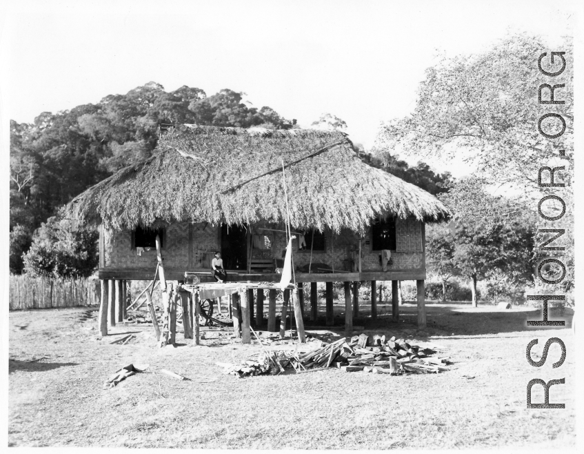 A woman sitting on the porch of a thatched-roof house on stilts in Burma.  Local people in Burma near the 797th Engineer Forestry Company.  During WWII.