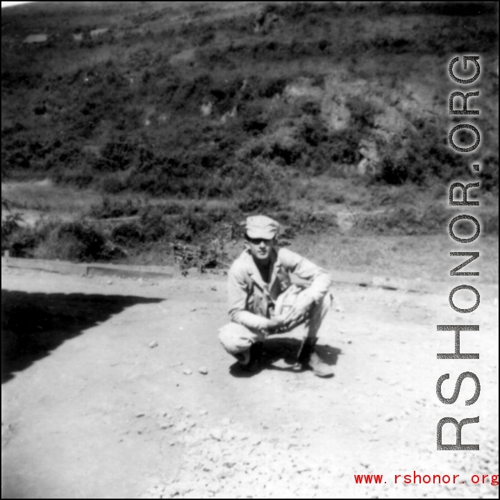 Douglas Runk squatting on road in SW China, during WWII.