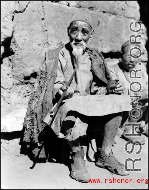 An elderly Chinese man at rest in the CBI, long pipe in hand.  From the collection of Wozniak, combat photographer for the 491st Bomb Squadron, in the CBI.