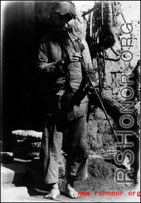 A man on the street in China, smoking a very long pipe, maybe Liuzhou or Yangkai.