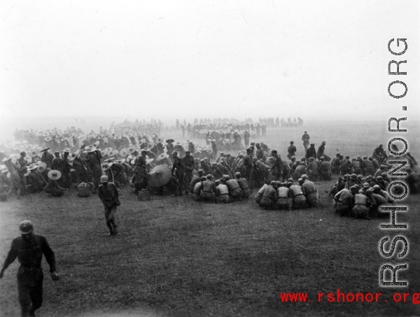 Chinese soldiers gathered in small groups to eat a meal in a pounding rain. During WWII.