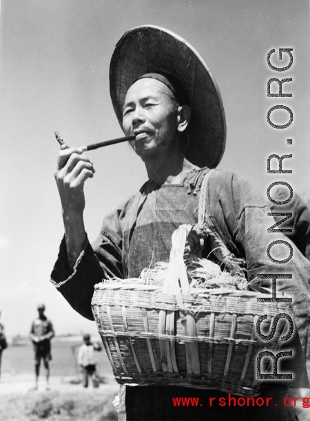 Local people in China: A farmer in the field smokes a short pipe. During WWII.