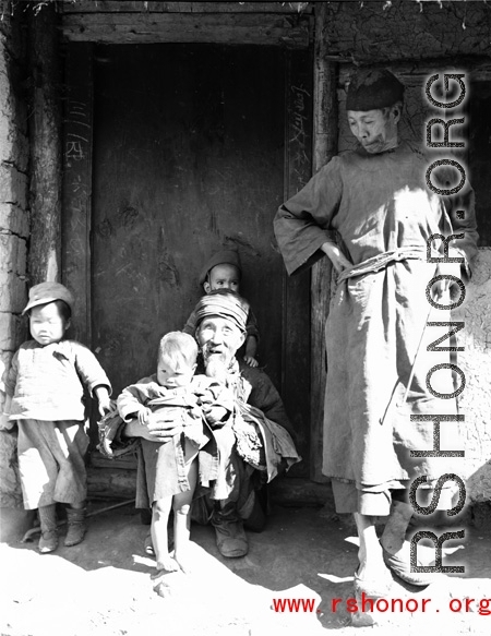 Local people in China: A poor elderly couple in a village watch over young children. During WWII.