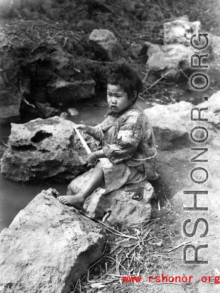 Impoverished kid sitting creekside in China during WWII.