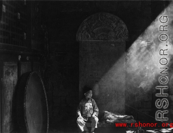 During WWII a boy sits in front of a stone tablet in the entry area of a temple or other building, probably in Yunnan province.