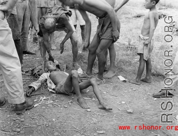 Concerned people (include at least to American GIs) surround a sick Chinese youth. The were many sick and weakened during the Chinese civilian evacuation in Liuzhou city, Guangxi province, China, during WWII, in the summer or fall of 1944 as the Japanese swept through as part of the large Ichigo push.