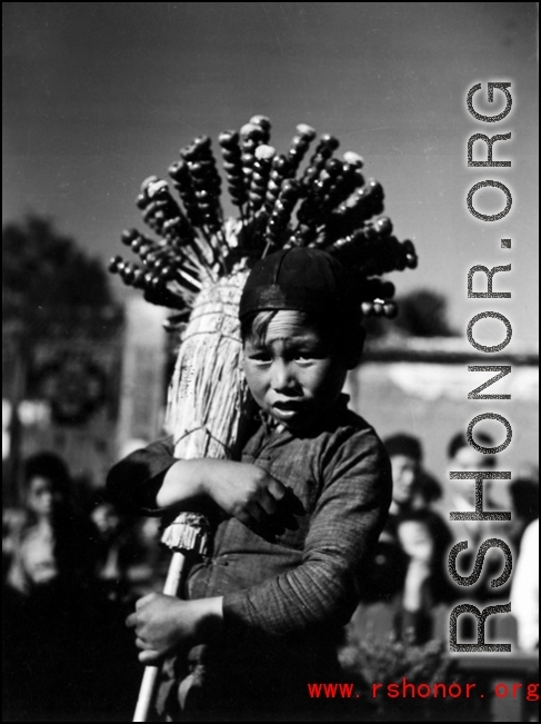 During WWII, a child sells candied fruit on the street, probably in Yunnan.  Local people in China, including a young candied fruit seller selling candied haws fruit on bamboo skewers.