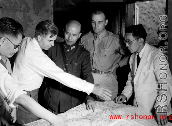 VIPs from both the US and China talk things over during WWII at a base somewhere in China.  Senator Henry Wallace gestures over the map, next to Chiang Kai-shek.