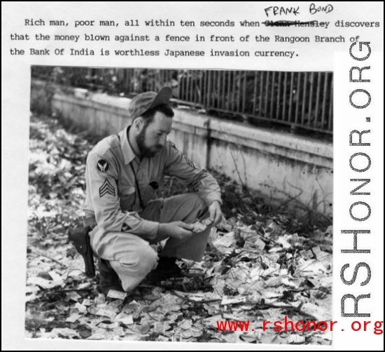 Frank Bond examines discarded "invasion currency" on a Rangoon, Burma, street near Bank of India, where it had been dumped during evacuation. Spring 1945.