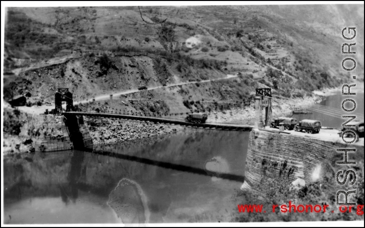 Trucks wait to cross a bridge on the Salween River one at a time. Note how the bridge bends down under the load of the transport truck going across. During WWII.