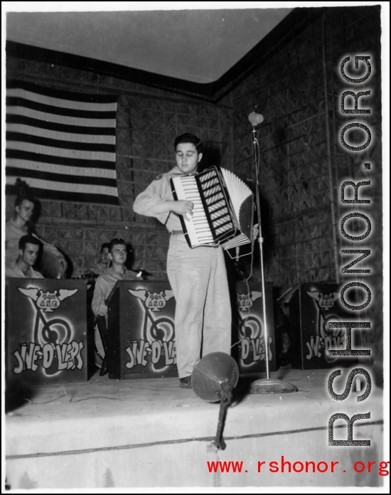 A GI plays accordian, while the "Jive-o-Lieps" of the 54th Air Service Group wait their turn In the CBI during WWII.