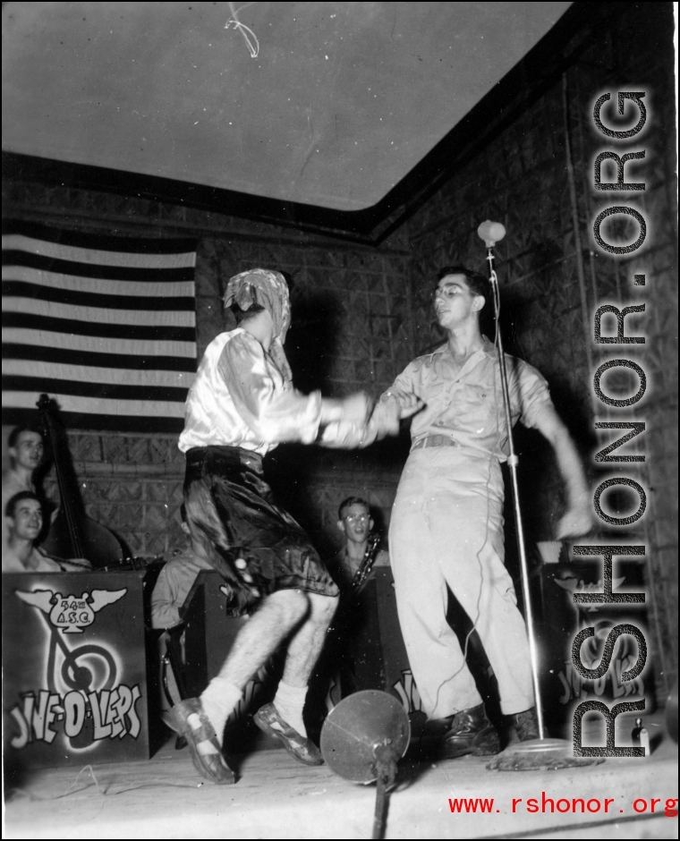 GIs perform at the microphone while musicians of the "Jive-o-Lieps" of the 54th Air Service Group watch on. In the CBI during WWII.