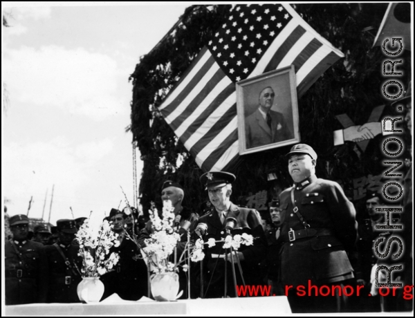 Burma Road dedication ceremony in Kunming, China, on February 4, 1945, during WWII. Review of first convoy (or one of the first convoys) to reach China. General view of the stage and reviewing party, with American and Chinese dignitaries, soldiers, and civilian VIPs. An American band plays, and an honor lines on both sides of the center carpet stand in formation.  Official dignitaries at the ceremony included, on the Chinese side, such figures as General Lung Yun, Governor of Yunnan Province,  Gen. Wang Yu-