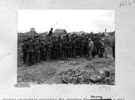 Chinese interpreter explaining the procedure for serving a meal to a group of Miao (ethnic) workers at the Laohwangping (Laohuangping) Airfield, China, in January, 1945. The control tower for the airbase can be see in the distance on the left.