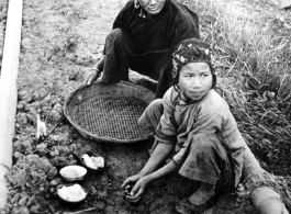 A Chinese woman and child start a fire next to a pipeline in which gasoline is flowing, 15 miles out of Kunming, next to the road to Chenggong (Chengkung). During WWII.