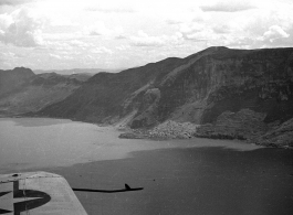 View over wing of Vultee SNV-2 (a variant of the BT-13) trainer piloted by Charles A. Breingan flys over Dianchi Lake (滇池) outside of Kunming, China, during WWII. Small boats dot the water surface, and a large landslide can be seen in the distance. 