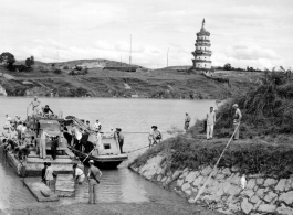 In this fascinating photo--a virtual Norman Rockwell still-life of wartime life in China--Chinese troops, American troops, and Chinese civilians cross the Xiao river (潇水) via ferry near Lingling, China, during WWII. In the background, on the east bank of the river, is the Huilong Pagoda (零陵回龙塔), which remarkably still survives, and has been restored.