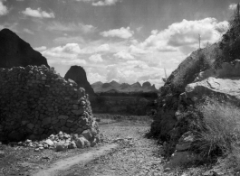 Karst mountains in the distance seen through an opening in a wall of stacked limestone. In Liuzhou, Guangxi, during WWII.