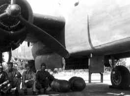 Jim, Frank Bates, Alex, Jim, 1943, in the shade under a B-25. Note large bombs on ground near them.