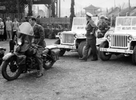 Burma Road dedication parade and ceremony in Kunming, China, on or around February 4, 1945, during WWII. Review of first convoy (or one of the first convoys) to reach China. General view of the stage area and MPs at the ready at jeeps provided by Service of Supply (SOS) .  The "Burma Road" was also often known as the "Stilwell Road," as it is in Chinese on the back of the stage, written “Shediwei Gonglu” (史迪威公路).