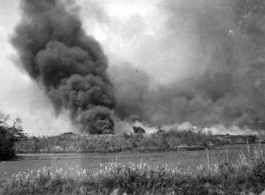 A smoke column arises, and smoke is widely spread about, at an American air base in China during WWII.