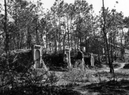 GI explorations of the hostel area at Yangkai air base during WWII: A GI walks past graves next to hostel buildings.