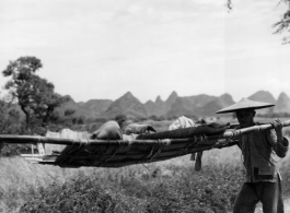 Men shoulder stretcher with injured or sick person in Guangxi, China, during WWII.