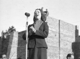 Opera singer Lilly Pons sings at a USO show in Gushkara, India, during WWII.  The boxes in front of the band players are labeled 748th ROB (748th Railway Operating Battalion).