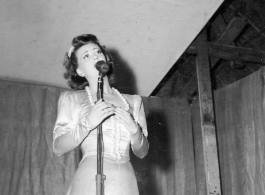 Singer at a USO show in Gushkara, India, during WWII.  The boxes in front of the band players are labeled 748th ROB (748th Railway Operating Battalion).