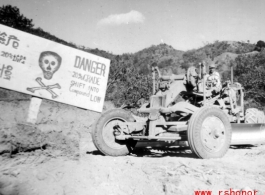 GI driving a road grader next to sign about an extremely dangerous stretch of Burma Road, at 20% grade! In Yunnan, China, or Burma. During WWII.