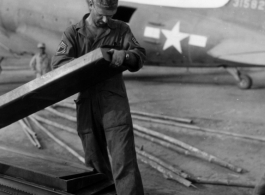 American GI working on air supply with C-47 in the background, and a Chinese worker standing nearby.