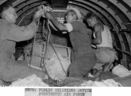 Bundles to be dropped by parachute are being tied to static line. The chutes will open automatically when kicked from the doorway to besieged Chinese troops by members of the Fourteenth Air Force Transport Unit.