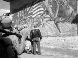 Americans and Chinese stop to look at a large wall mural showing peoples from four countries (China, Britain, United States, Russia, as shown by the four flags) uniting to put fascists in their place.