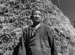 A blind villager in China poses for photographer with a stack of rice straw behind. During WWII.
