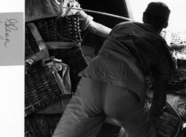 Men push woven baskets, with attached parachutes, out of a cargo plane mid air as part of an air drop in the CBI.   Photo from Glenn Hensley.