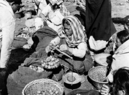 Women weight out produce for sale at a farmer's market in the CBI during WWII.