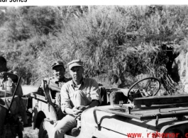 GI and Chinese soldier sit in a jeep, as a worker carries gear during WWII. Probably in Yunnan, China.