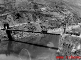 Trucks wait to cross a bridge on the Salween River one at a time. Note how the bridge bends down under the load of the transport truck going across. During WWII.