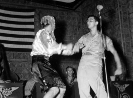 GIs perform at the microphone while musicians of the "Jive-o-Lieps" of the 54th Air Service Group watch on. In the CBI during WWII.