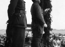 Chinese Lt. General Du Yuming, commander of Nationalist 5th Corps (第五集团军总司令兼昆明防守司令杜聿明) looks out at troops, with Gen. Wei Lihuang (卫立煌) facing assembled troops, and another person holding a sheet of paper, on stage during rally.