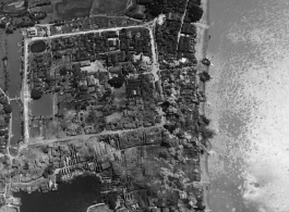 B-25 Mitchell bombers bomb a small town along a river in the CBI.  Note the squaire remnants of a historic city wall. The town shows previous bomb or war damage.